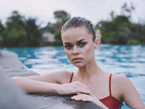 portrait of a woman in a red swimsuit near the tiles of the pool landscape bushes trees - Photo, Image