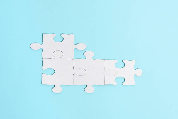 Close-Up White Jigsaw Pattern Puzzle Pieces To Be Connected With Missing Last Piece Positioned On A Flat Lay Background With Different Texture And Paper Supplies Accesories - Foto, afbeelding