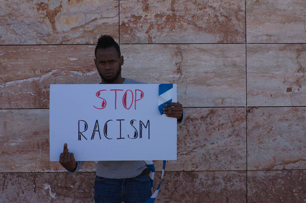 Un hombre afroamericano en una pared sostiene un letrero que dice "Alto al racismo". El hombre lleva una bandera alemana sobre sus hombros.. - Foto, Imagen