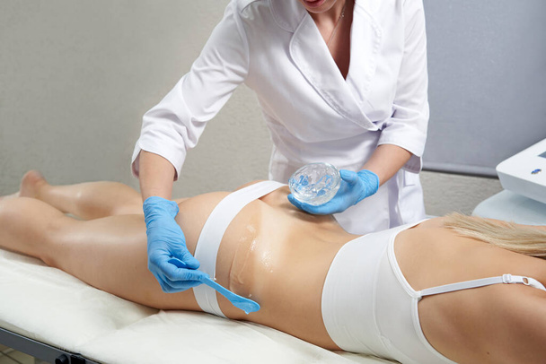 косметолог наносит прозрачный гель на ноги и ягодицы пациентов для косметического лечения - Фото, изображение