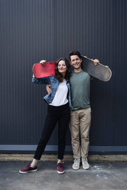 Современная улыбающаяся пара, стоящая вместе со скейтбордами - Фото, изображение