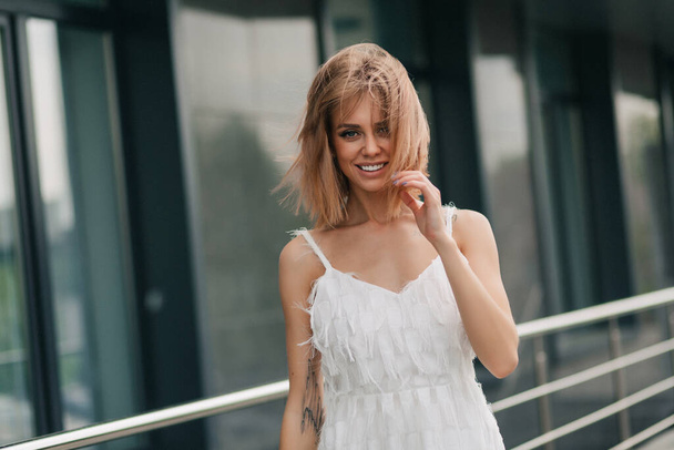 Close up portrait of charming blond girl wearing white dress with loose hair smiling at camera. High quality photo - Φωτογραφία, εικόνα