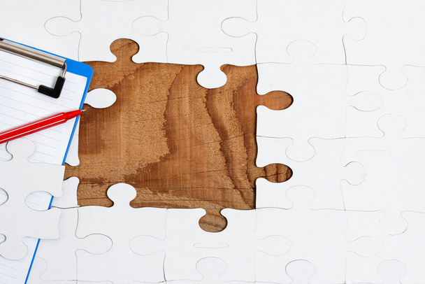 Close-Up White Jigsaw Pattern Puzzle Piezas que se conectarán con faltante última pieza colocada en un fondo plano con diferentes accesorios de textura y papel - Foto, imagen