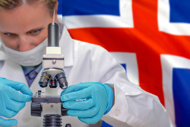 Женщина-биохимик смотрит в микроскоп на фоне флага Исландии. Медицинские технологии и фармацевтические исследования и разработка концепции науки в Исландии - Фото, изображение