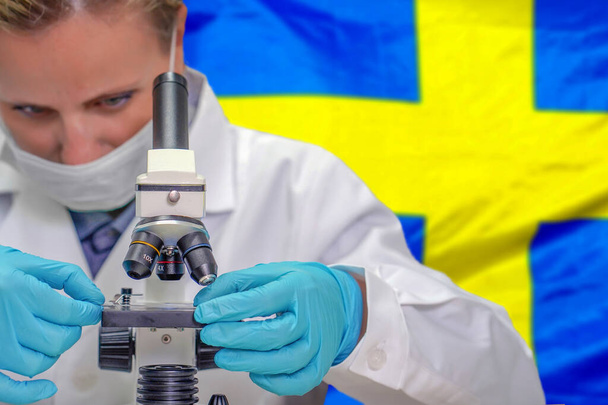 Biochimiste féminine regardant à travers un microscope sur fond de drapeau suédois. Technologie médicale et recherche pharmaceutique et développement de concepts scientifiques en Suède - Photo, image