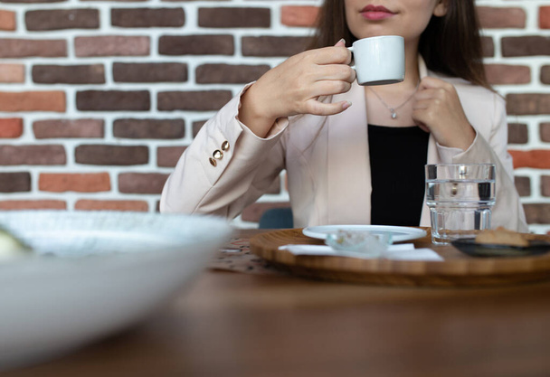 Girl in jacket drinks coffee against brick wall. - Foto, imagen