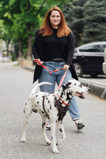 Femme marchant, discutant et jouant avec son animal de compagnie dalmate en ville - Photo, image