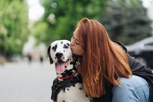 Pretty woman kissing dalmatian dog on street city background - Φωτογραφία, εικόνα