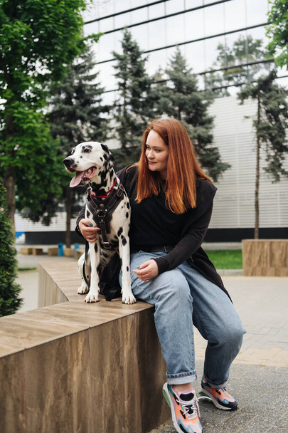ładna kobieta pozowanie i przytulanie dalmatyński pies na ulicy tło miasta - Zdjęcie, obraz