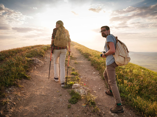 A couple of happy young hikers backpacking on a beautiful rocky trail on a warm, sunset evening. The concept of family travel and adventure. view from behind. Travel lifestyle. - Photo, Image