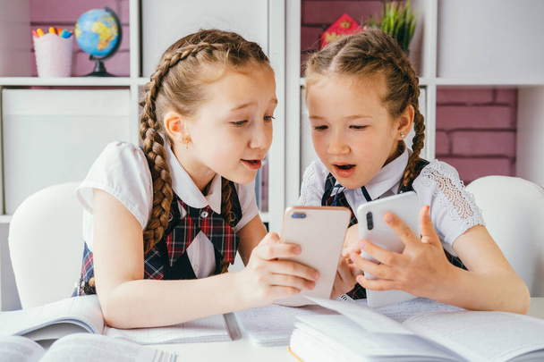 Zwei junge Mitschülerinnen sitzen an einem Schreibtisch und nutzen Smartphones. Modernes Technologiekonzept. - Foto, Bild
