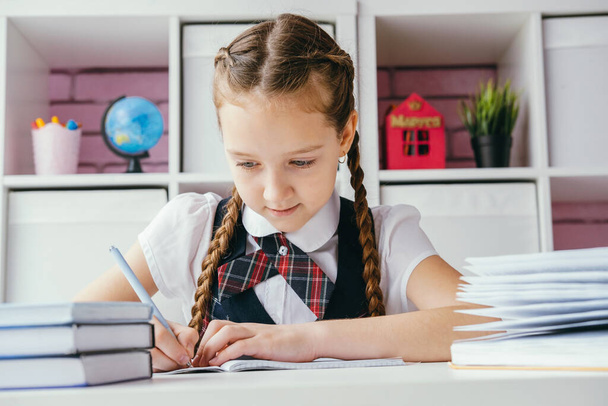 Portrait beautiful positive little schoolgirl sitting at her desk and doing her homework. Back to school concept. - Фото, зображення