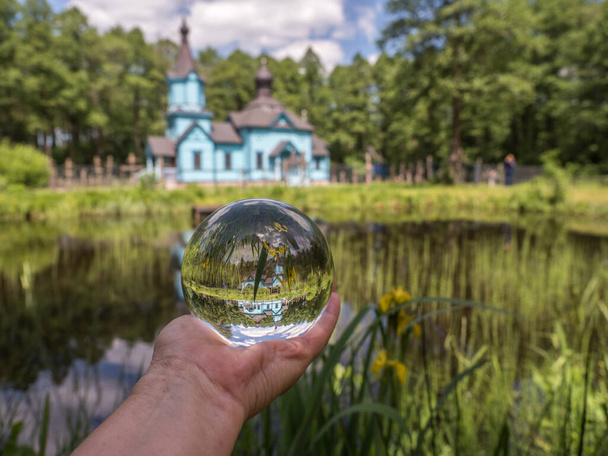 Koterka, Polen - 20 mei 2018: Blauwe, houten orthodoxe kerk en kerk reflecterend in de glazen bol en in de vijver, in het voorjaar. Podlachia-regio, - Foto, afbeelding