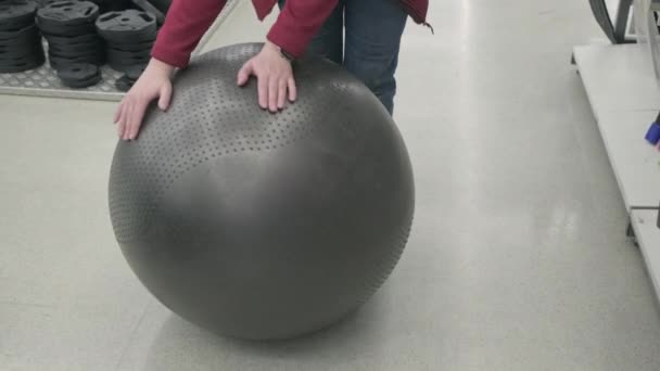 Bir spor mağazasındaki kadın siyah bir fitball topu alır. Üzerine oturdu ve atladı. - Video, Çekim