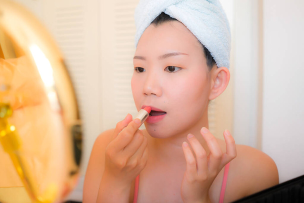 young Asian woman applying makeup - beautiful and attractive Korean girl with head towel putting facial make-up at home in the morning in beauty and fashion concept - Photo, Image