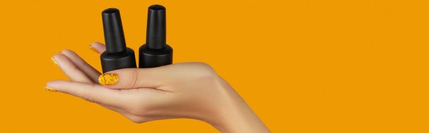 Manicured womans hand holding nail varnish bottle on orange background. Beauty salon template - Photo, Image