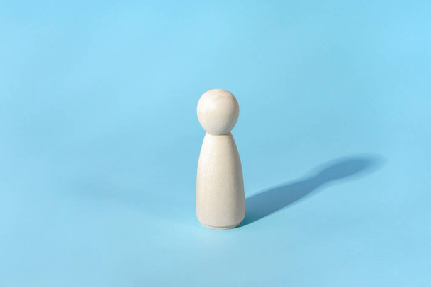 Abstract concept of lonely person. Minimalist, wooden figure with shadow on blue - Photo, Image