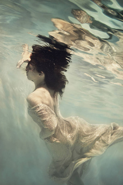 A girl in a long dress with sequins flies under water as if in weightlessness - Foto, Imagem