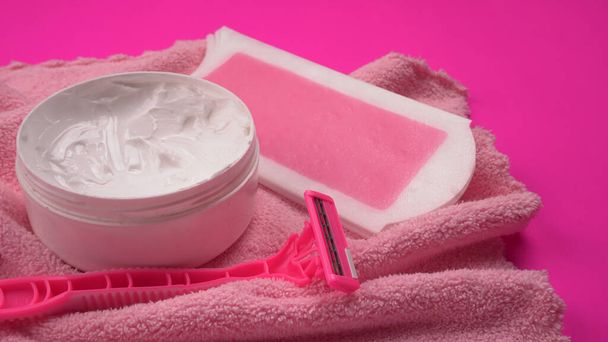 Viaszcsíkok közelsége tejszínhabbal és rózsaszín eldobható borotvával a női bőr színes törölközőn történő biztonságos borotválásához, női szőrtelenítés koncepciója - Fotó, kép
