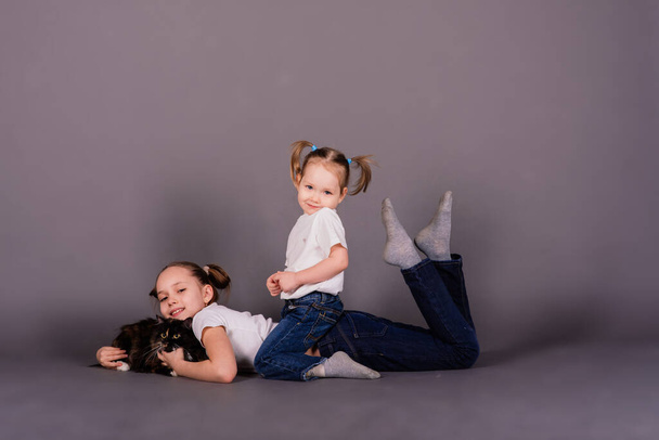 Two girls sisters hugging black cat in a studio - Photo, Image
