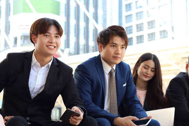 Egy csoport fiatal ázsiai boldog üzletember szocializálódik, miközben a modern belvárosban ülnek a lépcsőn. üzletemberek beszélgetnek és beszélgetnek.  - Fotó, kép