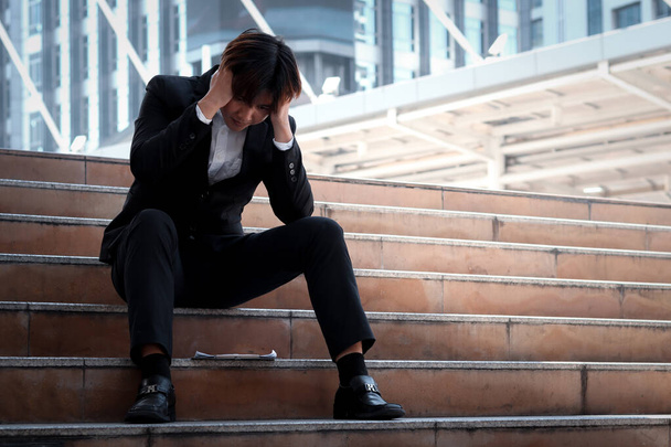 Stresli genç Asyalı iş adamı şehir merkezindeki ofisin merdivenlerinde oturuyor. Adam kafasını eline koyar işini düşünür, kendini hayal kırıklığına uğramış ya da yorgun hisseder.. - Fotoğraf, Görsel