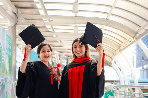 Δύο ευτυχείς χαμογελαστοί απόφοιτοι φοιτητές, νέες όμορφες Ασιάτισσες γιορτάζουν την επιτυχή εκπαίδευση γιορτάζοντας ρίχνοντας τετράγωνο ακαδημαϊκό καπέλο την ημέρα αποφοίτησης (ημέρα έναρξης), όταν έχουν τελειώσει τις σπουδές για το πανεπιστήμιο ή το κολέγιο. - Φωτογραφία, εικόνα