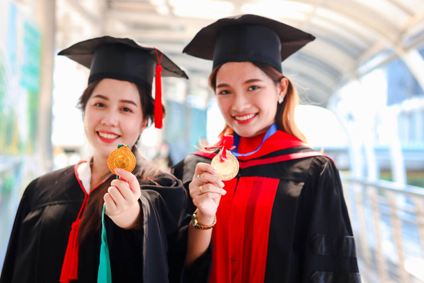 Портрет двох радісних усміхнених студентів, які мають золоту медаль, молодих красивих азіатських жінок, які дивляться на камеру так пишаються в день їх початку, люди, які відзначають успішну освіту в день випуску, коли закінчують навчання для uni - Фото, зображення