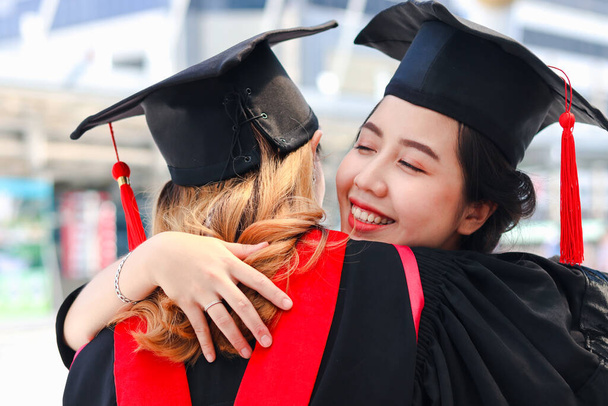 Две счастливые выпускницы студентки с квадратной академической шляпкой обнимают друг друга, люди празднуют успешное образование и поздравляют с Днем начала выпускного, когда закончат учебу в университете или колледже. - Фото, изображение
