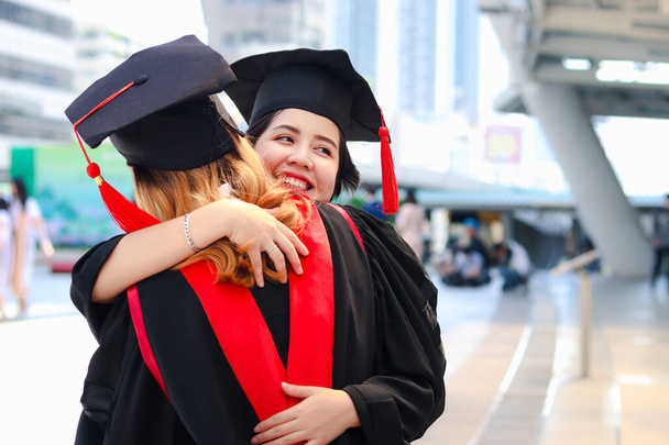 Dvě šťastně absolvované studentky se čtvercovým akademickým kloboukem objímající se navzájem, lidé oslavující úspěšné vzdělání a blahopřejí s kamarádkou k zahájení absolventského dne, kdy dokončili studium na vysoké škole nebo. - Fotografie, Obrázek