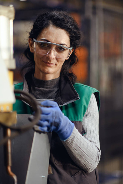Woman worker wearing safety goggles control lathe machines to drill components. Metal lathe industrial manufacturing factory. High quality photo - Foto, Bild