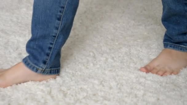 Pequeño chico descalzo en jeans caminando sobre una suave alfombra blanca en casa - Metraje, vídeo