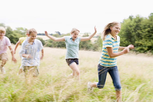 Five young friends running in a field smiling - Foto, afbeelding