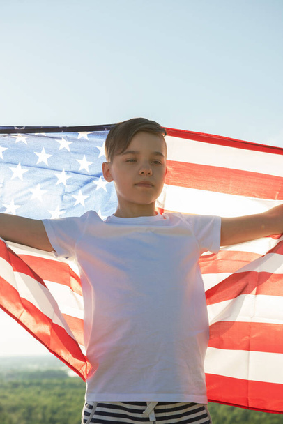 Menino loiro acenando bandeira nacional dos EUA ao ar livre sobre o céu azul na margem do rio - Foto, Imagem