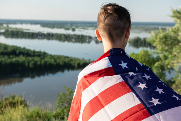 Blonďatý chlapec mává národní vlajkou USA venku nad modrou oblohou na břehu řeky - Fotografie, Obrázek