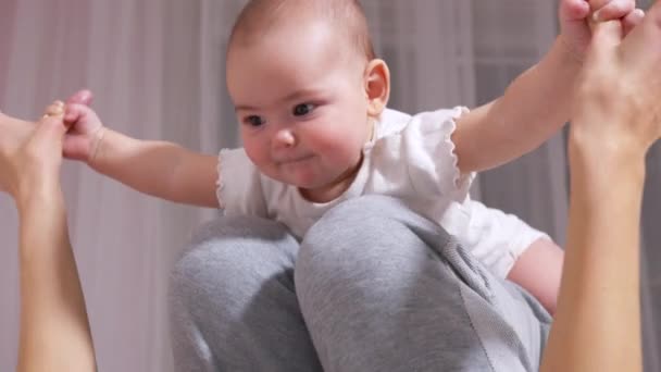 Happy healthy young adult mom lifting cute infant child daughter up playing airplane on bed. Любящая мама делает гимнастические упражнения йоги со смешным обожаемым ребенком в уютной спальне. - Кадры, видео
