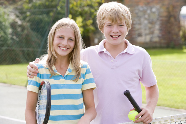 Young couple with rackets on tennis court smiling - Foto, afbeelding