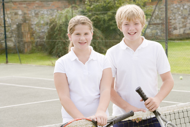 Two young friends with rackets on tennis court smiling - Фото, изображение