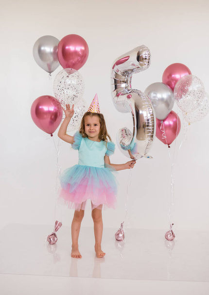 little girl in a festive dress with a tutu skirt holds balloons on a white background with a copy of the space. Birthday Celebration - Photo, Image