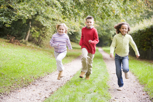 Three young friends running on a path outdoors smiling - Zdjęcie, obraz