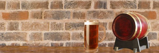 mug of foamy beer and barrel on wooden table near brick wall with place for text - Fotoğraf, Görsel