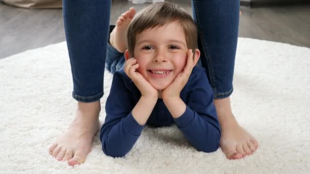Portret van gelukkig lachend jongetje liggend op tapijt tussen moeders voeten - Video