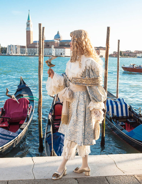 Venedik, İtalya - 20 Şubat 2020: Karnavaldaki adam karnaval, gondol ve Aziz George Manastırı 'nda toplandı ve maskelendi. - Fotoğraf, Görsel