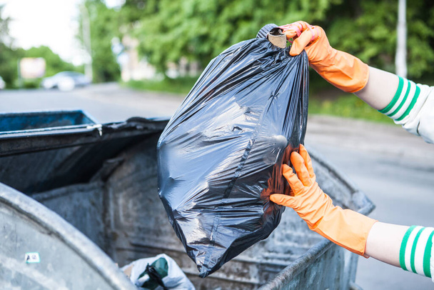 Cropped close up of a person putting garbage bag into trash can on city street - 写真・画像