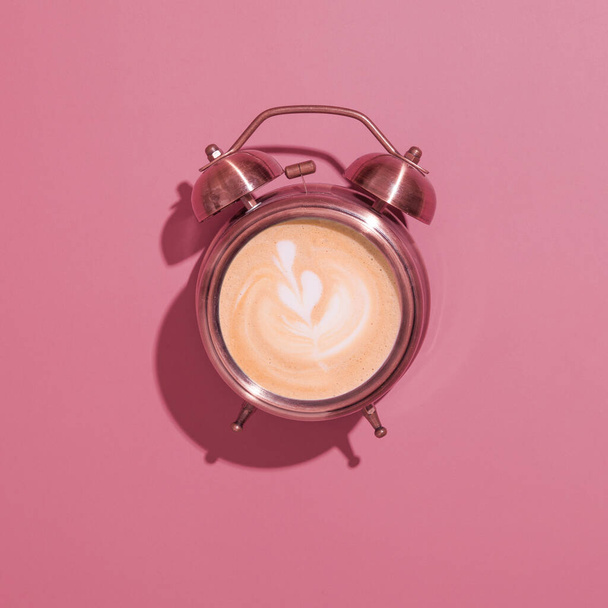 Reloj despertador encendido con café espumoso y patrón. Sombras duras. Salida de la mañana con café para el desayuno concepto  - Foto, imagen