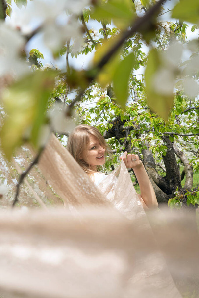 Молодая, красивая, весёлая женщина гуляет в солнечный весенний день на природе под цветущими вишнями в красивом женском наряде. - Фото, изображение