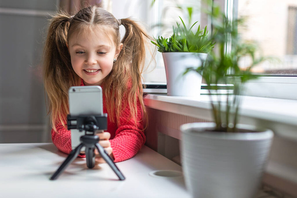Happy little girl using telephone, smiling at screen, communicates online at home, talking via video call, watching movie or online lesson. Generation Z concept - Photo, image