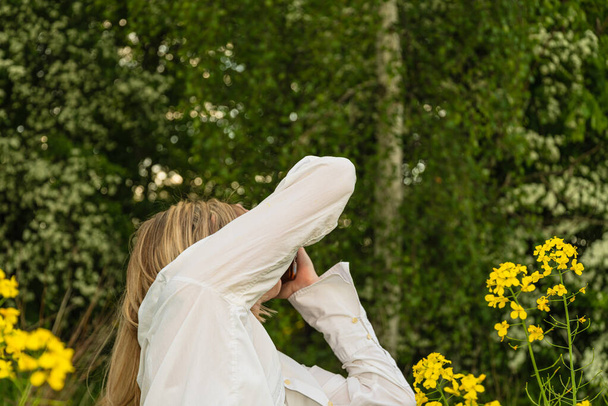 A girl in a white shirt covers her head with her hands on a background of a green forest - Foto, imagen