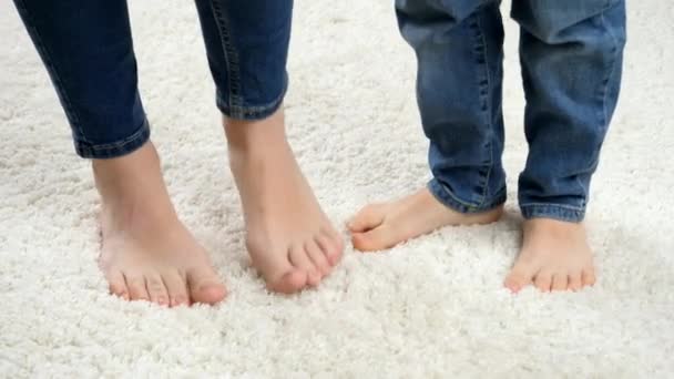 Close-up van kinderen voeten dansen met moeders voeten op wit zacht tapijt. - Video