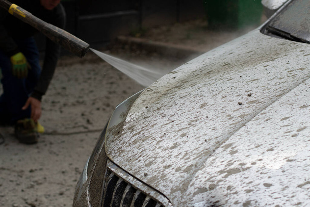 Car wash. The car is washed under the pressure of a jet of water. Using a water spray to wash off dirt from the surface of the car. - Φωτογραφία, εικόνα